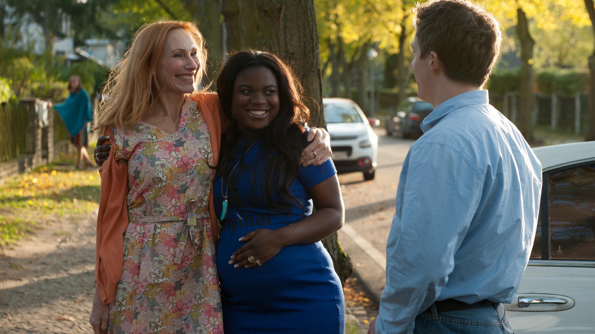 Gundula (Andrea Sawatzki) hält Candy (Ludie Diekumpovisa) auf der Straße im Arm, davor steht Rolfi (Oskar Bökelmann) und schaut die beiden an.