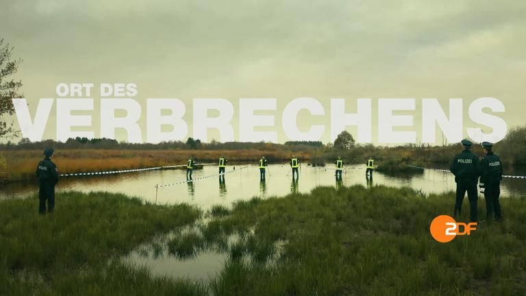 Ein herbstliches Moor unter grauem Himmel. Im Wasser stehen mehrere Personen in Schutzkleidung, die nach etwas im Wasser stochern. Auf der Wiese am Rand drei Polizisten in Uniform. Am Himmel ist der Schriftzug "Ort des Verbrechens" in weiß zu lesen.