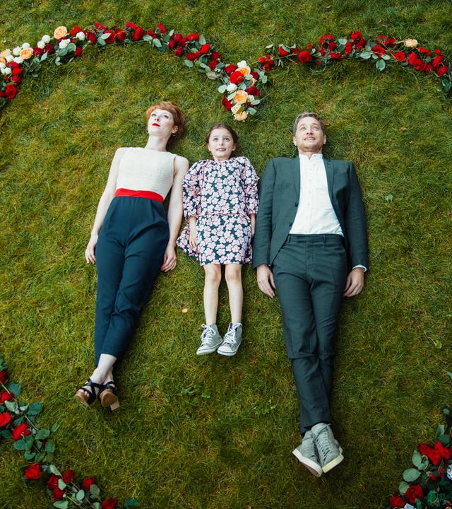 Lena (Sarah Bauerett), ihre Pflegetochter Talisa (Filippa Möller) und ihr Verlobter Marek (Markus “Maeckes” Winter) machen das Foto für ihre Hochzeitseinladungskarte. Dafür liegen sie auf dem Rasen, in einem Herz aus Rosen.
