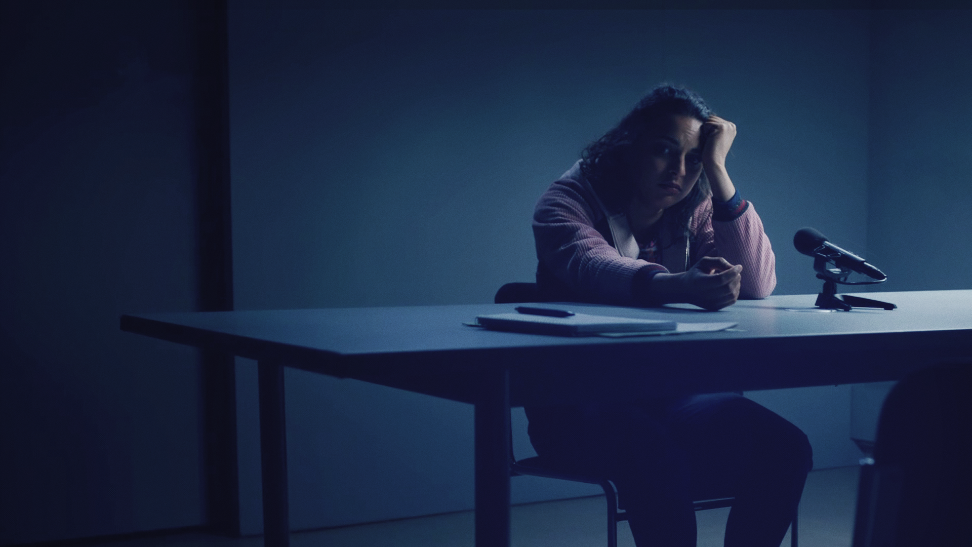 Eine Frau in einem spärlich beleuchteten Verhörzimmer der Polizei. 
