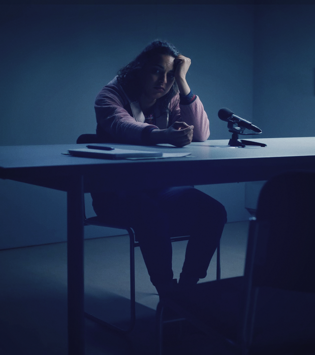 Eine Frau in einem spärlich beleuchteten Verhörzimmer der Polizei. 