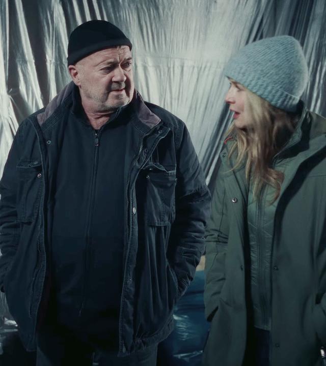 Die Kommissare Otto und Linett (Florian Martens, Stefanie Stappenbeck) stehen in Winterkleidung und Mützen vor einer Wand, die mit Plastikfolie verhängt ist.