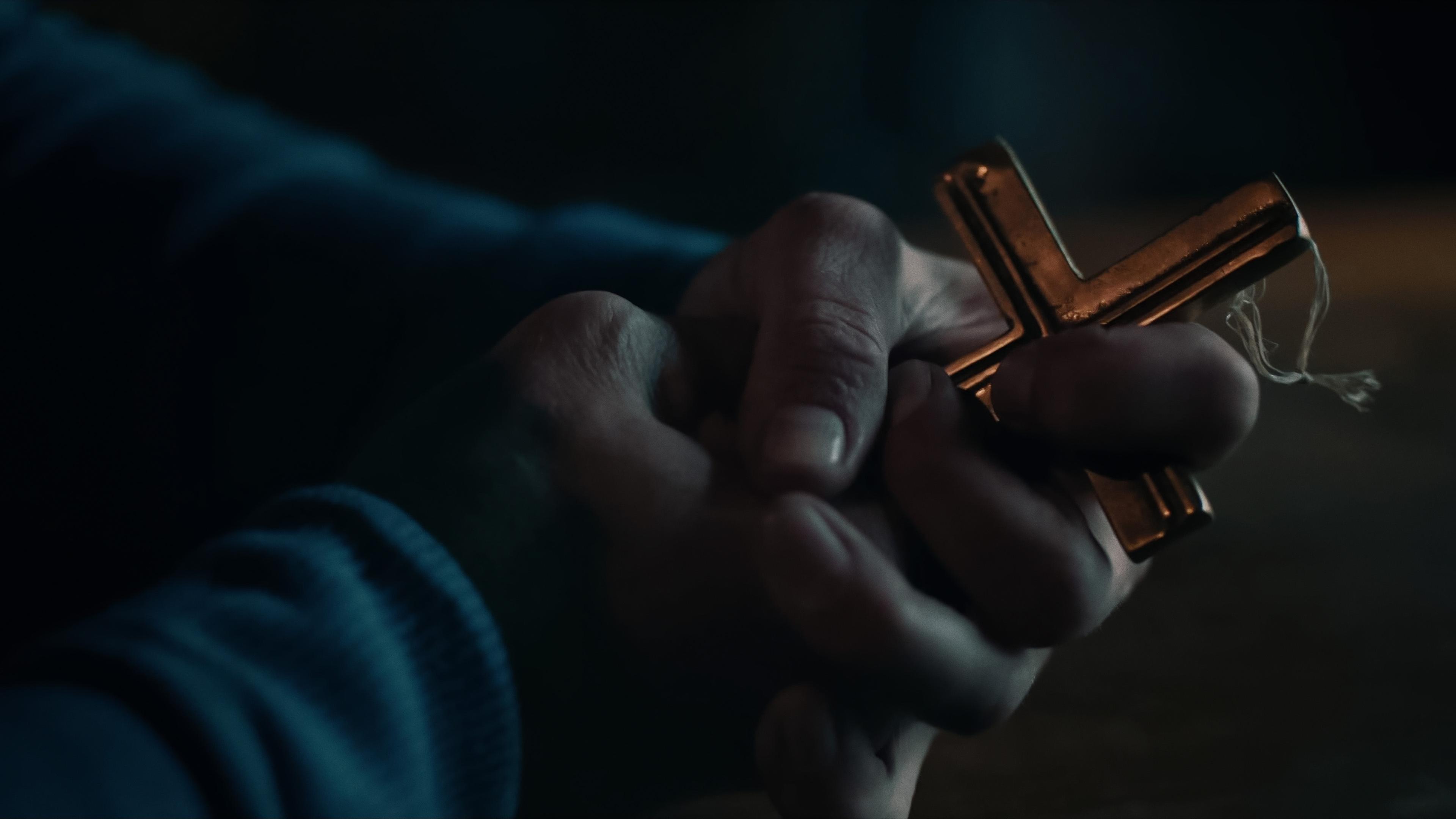 Ein christliches Kreuz aus Bronze wird fest von zwei Händen ergriffen. 