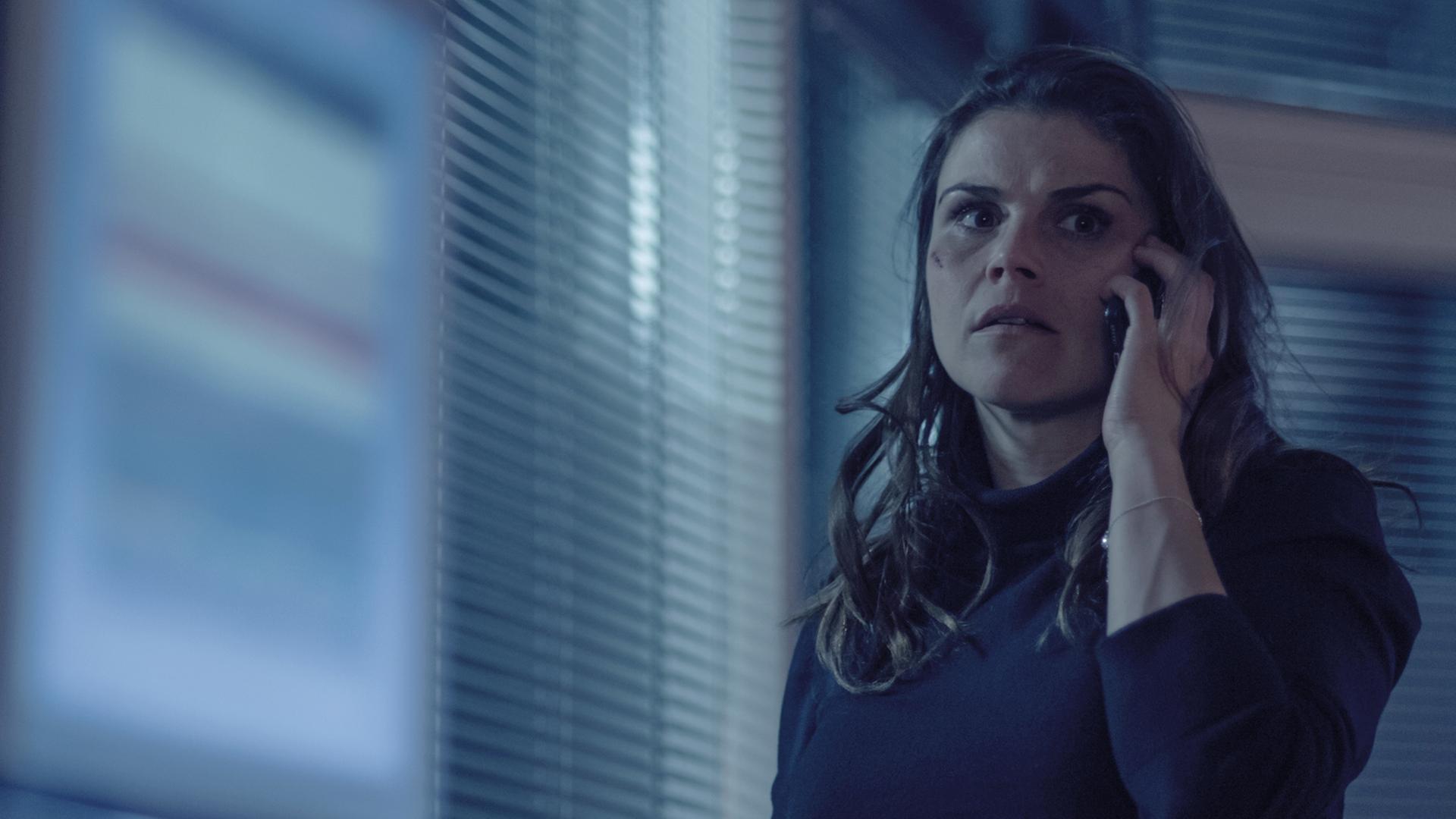 Nina Petersen (Katharina Wackernagel) steht im Büro und telefoniert. Sie sieht angespannt aus, unter dem rechten Auge hat sie eine Verletzung wie von einem Faustschlag.