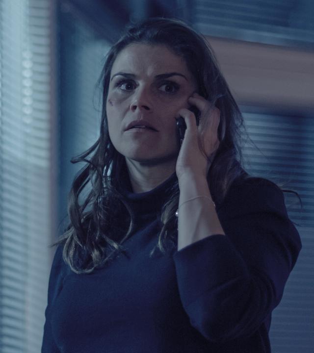 Nina Petersen (Katharina Wackernagel) steht im Büro und telefoniert. Sie sieht angespannt aus, unter dem rechten Auge hat sie eine Verletzung wie von einem Faustschlag.
