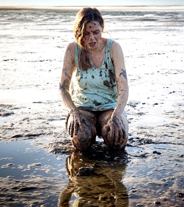 Ann Kathrin Klaasen (Picco von Groote) kniet im Watt nur mit einem Hemd bekleidet. Sie ist über und über mit Schlamm verschmiert. Sie schaut entsetzt auf ihre Knie: Überall auf ihrem Körper sind Tattoos.