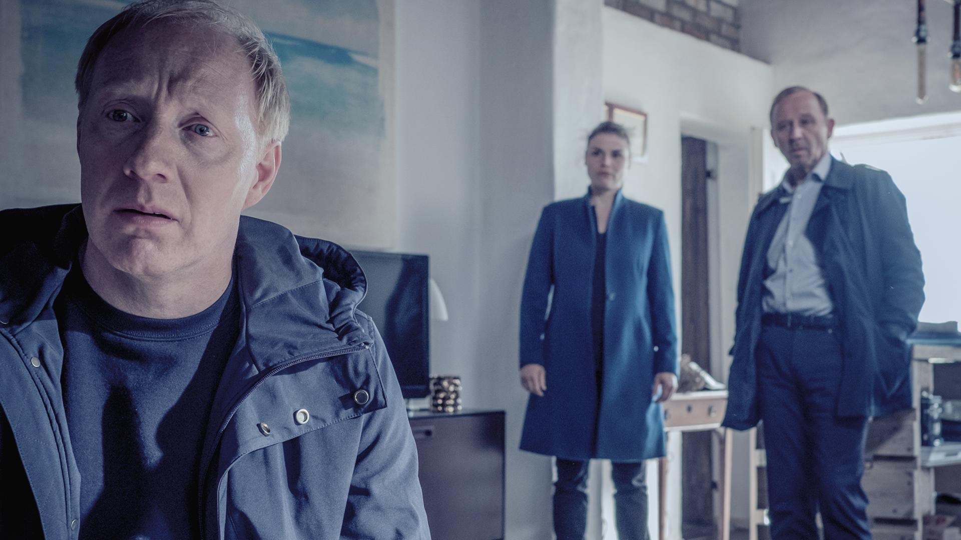 Peter Thies (Simon Schwarz), ein rotblonder Mann mittleren Alters, sitzt in seiner Wohnung und schaut verzweifelt. Im Hintergrund Nina Petersen (Katharina Wackernagel) und Karl Hidde (Alexander Held)