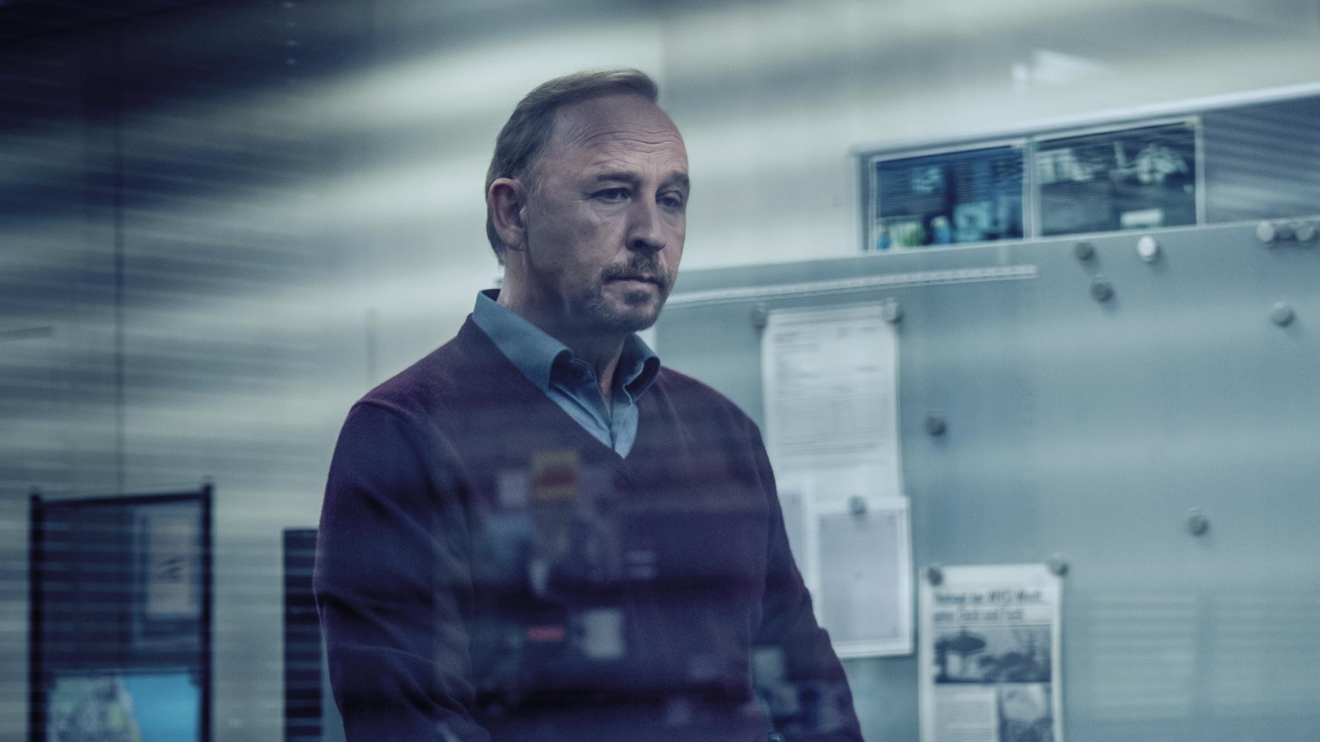 Karl Hidde (Alexander Held) steht nachdenklich im Büro. 