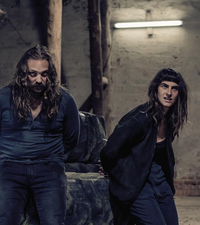 Hanne Beckmann (Samia Chancrin) und Peter Gruber (Denis Schmidt) stehen in einer Scheune. Vor ihnen zwei Polizisten, die nur von hinten zu sehen sind. 