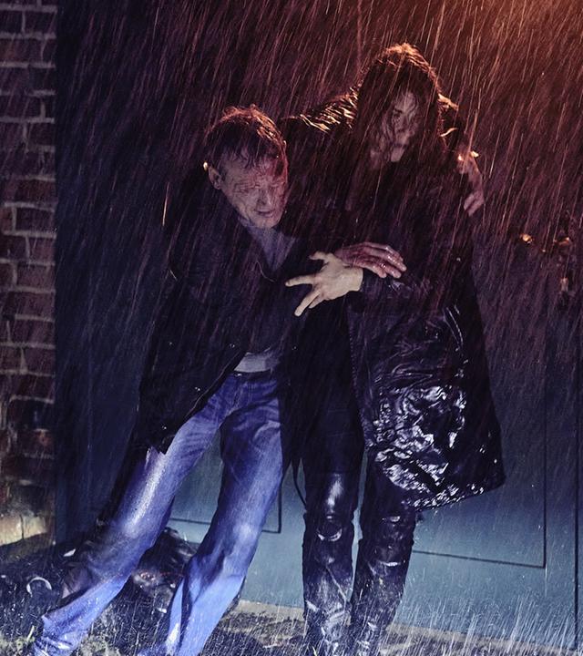 Nina Petersen (Katharina Wackernagel) stützt den am Kopf blutenden Benjamin Lietz (Wotan Wilke Möhring) auf dem Weg zum Auto. Es ist nacht und regnet stark.