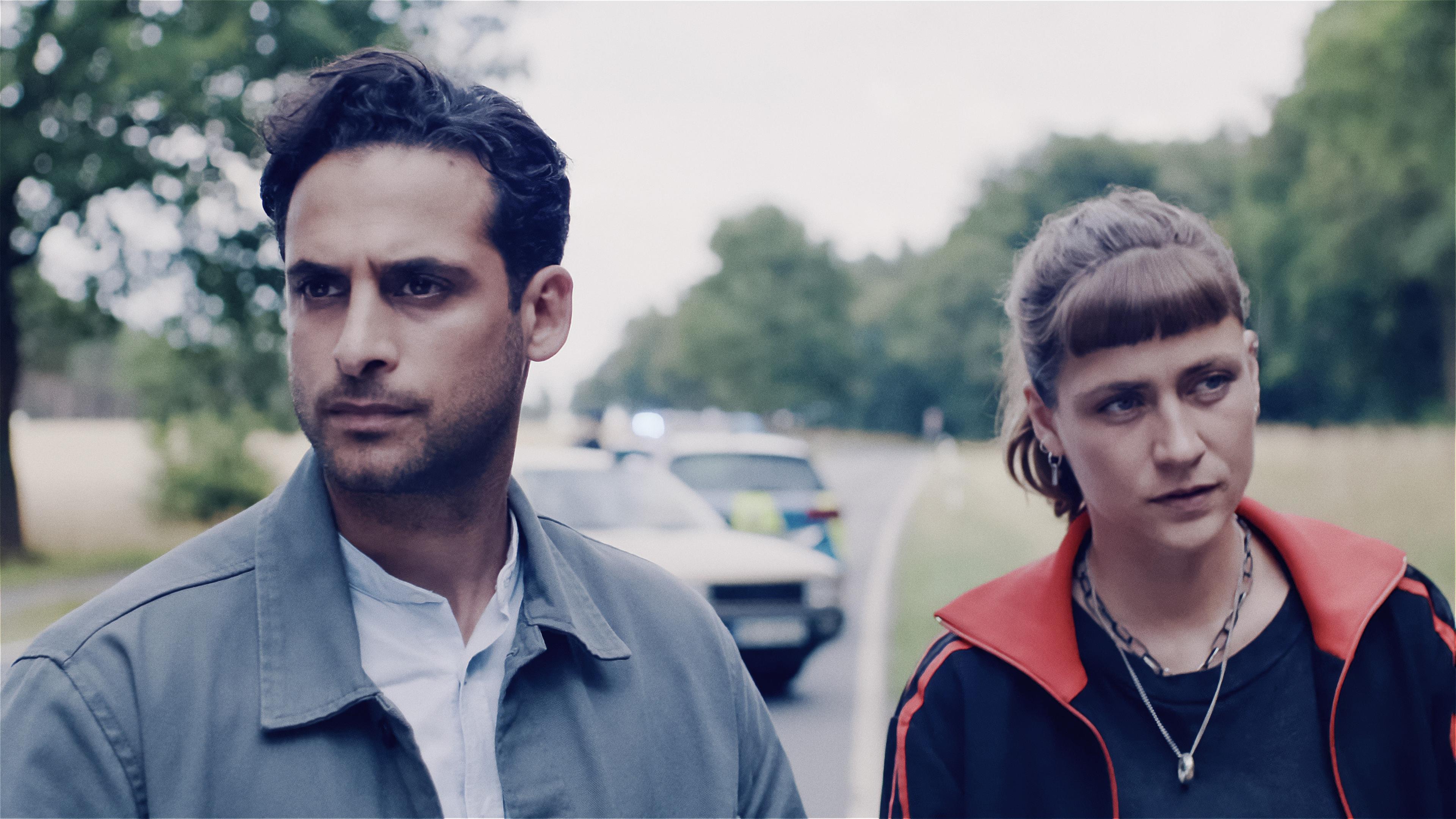 Karim Uthman (Karim Günes) und Jule Zabek (Sophie Pfennigstorf) stehen auf einer Landstraße. Hinter ihnen ein verunglücktes Auto und ein Polizeiauto mit Blaulicht. Beide schauen nachdenklich nach vorn.