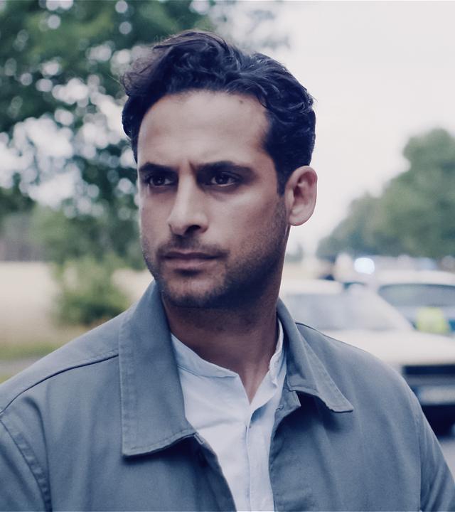 Karim Uthman (Karim Günes) und Jule Zabek (Sophie Pfennigstorf) stehen auf einer Landstraße. Hinter ihnen ein verunglücktes Auto und ein Polizeiauto mit Blaulicht. Beide schauen nachdenklich nach vorn.