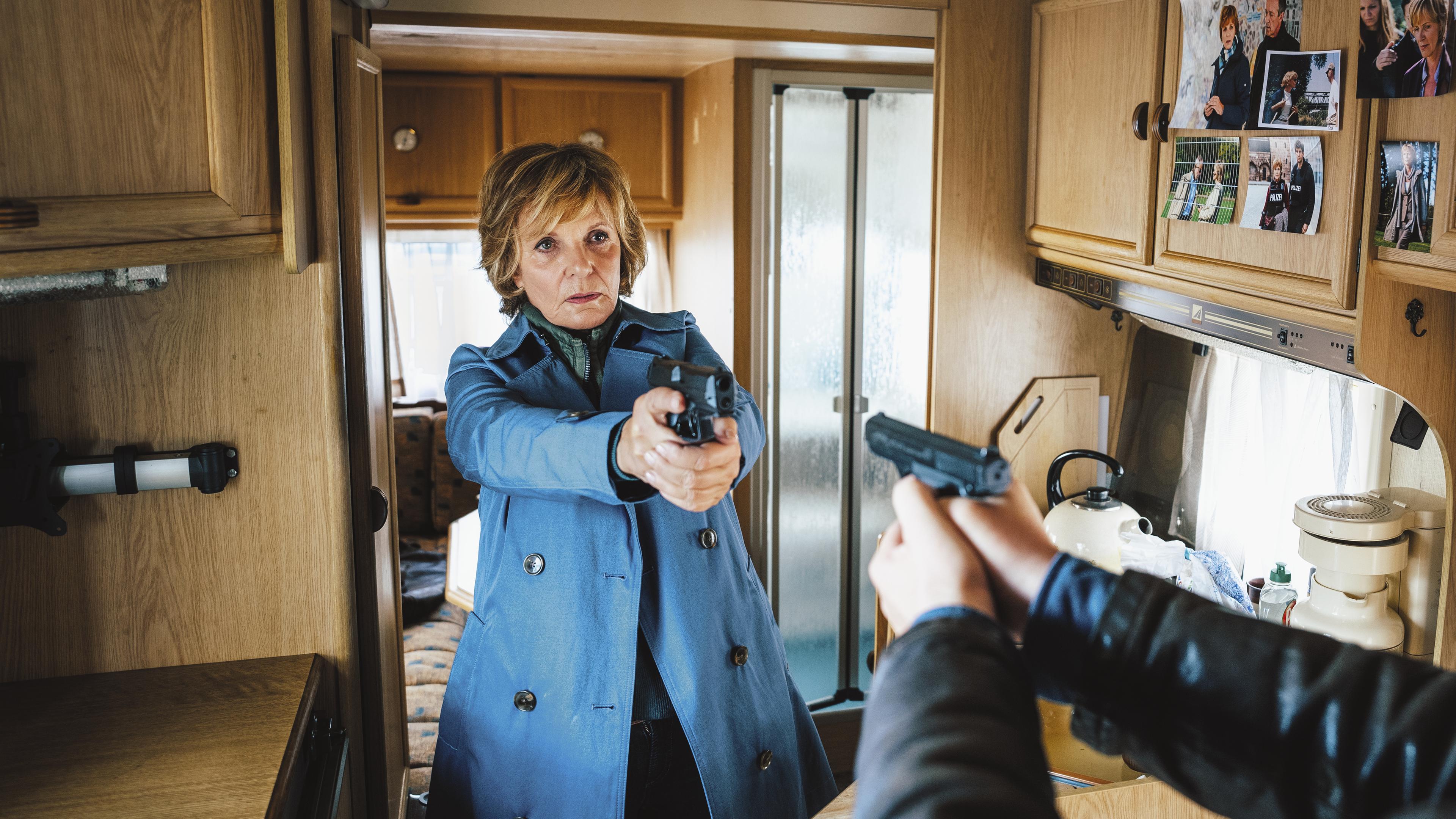 Kommissarin Lucas (Ulrike Kriener) und Kollege Wolfram Truss (Rainer Bock) stehen sich im Wohnwagen gegenüber und richten ihre Waffen aufeinander.
