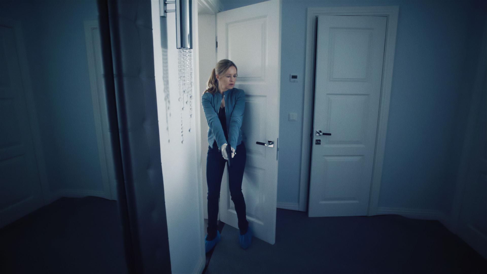 Linett (Stephanie Stappenbeck) steht in einer Wohnung. Vor sich hält sie ihre Waffe, leicht nach unten gerichtet, aber bereit zum Schuss.