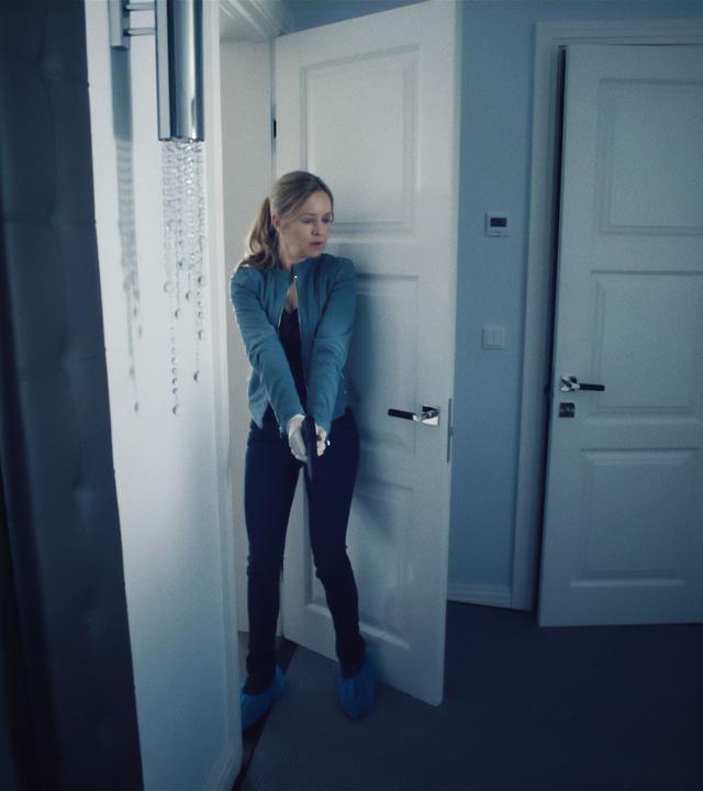 Linett (Stephanie Stappenbeck) steht in einer Wohnung. Vor sich hält sie ihre Waffe, leicht nach unten gerichtet, aber bereit zum Schuss.