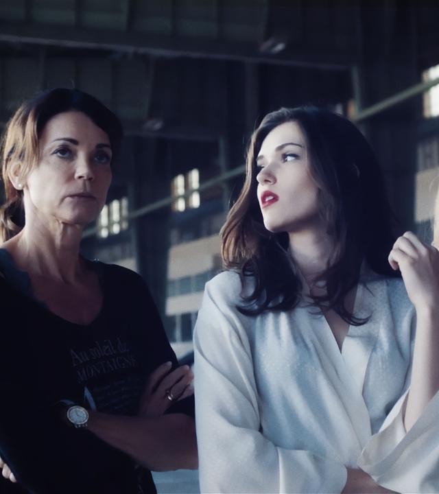 In einer industriellen Halle stehen drei Frauen und schauen genervt: Helen Weber (Gerit Kling), Hanna Weber (Caroline Hartig) und Leonie Seiters (Amelie Otto). Hanna und Leonie haben beide auffällig rot geschminkte Lippen und tragen weiße Morgenmäntel - offenbar sind sie als Models da.