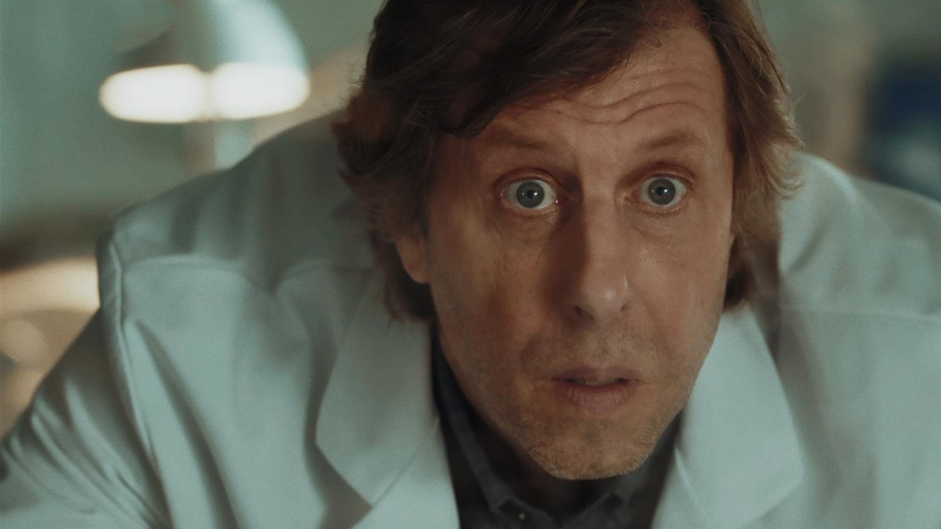 Ekki (Oliver Korittke) in einem weißen Laborkittel, sein Gesichtsausdruck erstaunt und geschockt. 