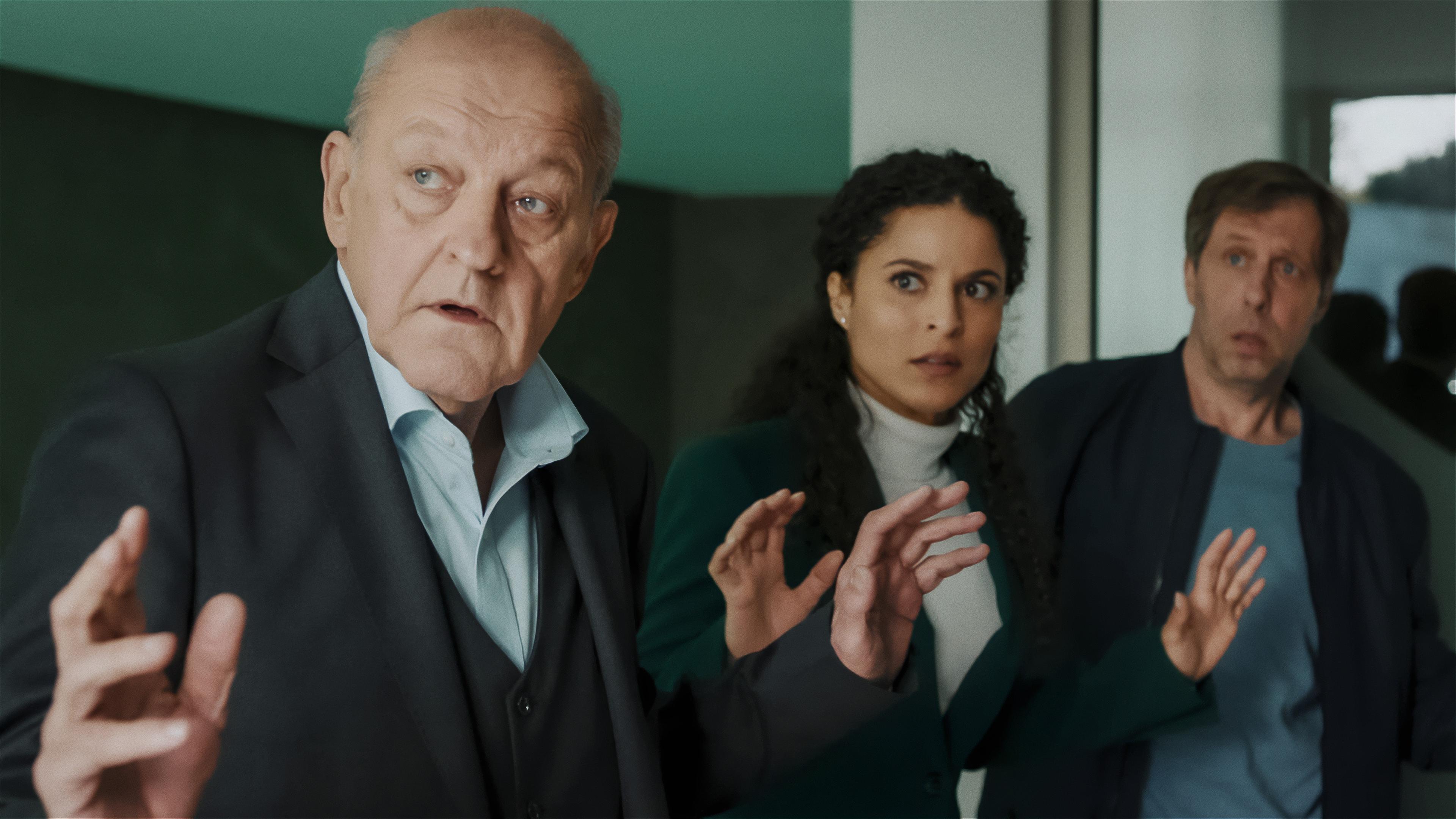 Georg Wilsberg (Leonard Lansink), Dr. Tessa Tilker (Patricia Meeden) und Ekki Talkötter (Oliver Korittke) stehen in einem Innenraum und haben die Hände erhoben. Alle drei schauen erschrocken nach links zu etwas oder jemandem außerhalb des Bildes.