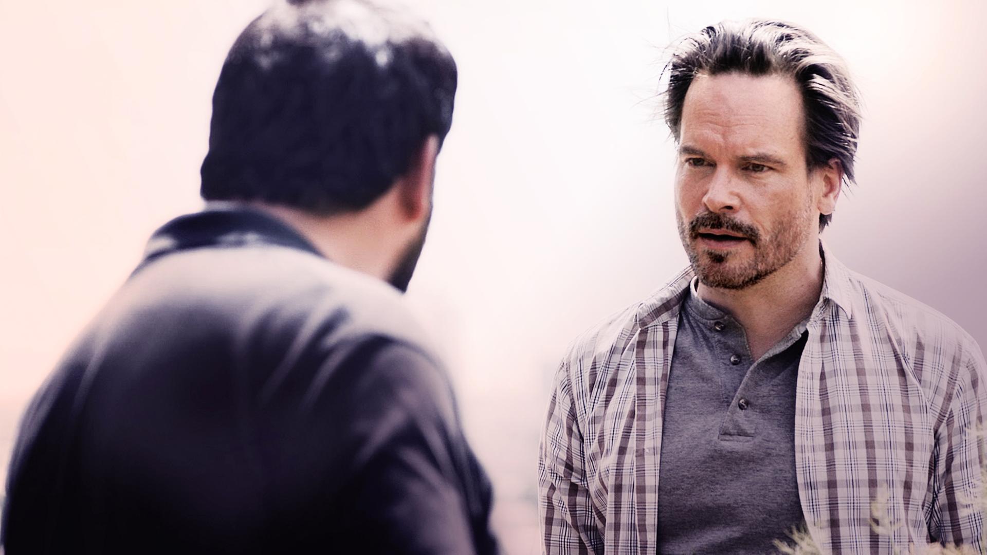 Leo Oswald (Wanja Mues) unterhält sich mit jemanden im Bildvordergrund, den man nicht erkennen kann. 