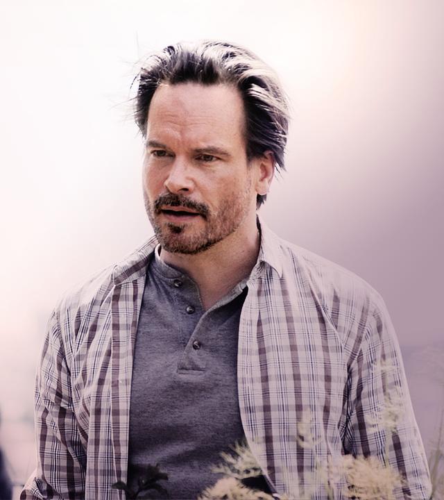 Leo Oswald (Wanja Mues) unterhält sich mit jemanden im Bildvordergrund, den man nicht erkennen kann. 