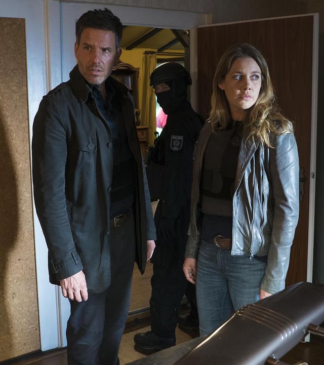 Oliver von Bodenstein (Tim Bergmann) und Pia Kirchhoff (Felicitas Woll) stehen in einem Zimmer und schauen sich überrascht um. Hinter ihnen ist ein Polizist in der offenen Tür zu sehen.