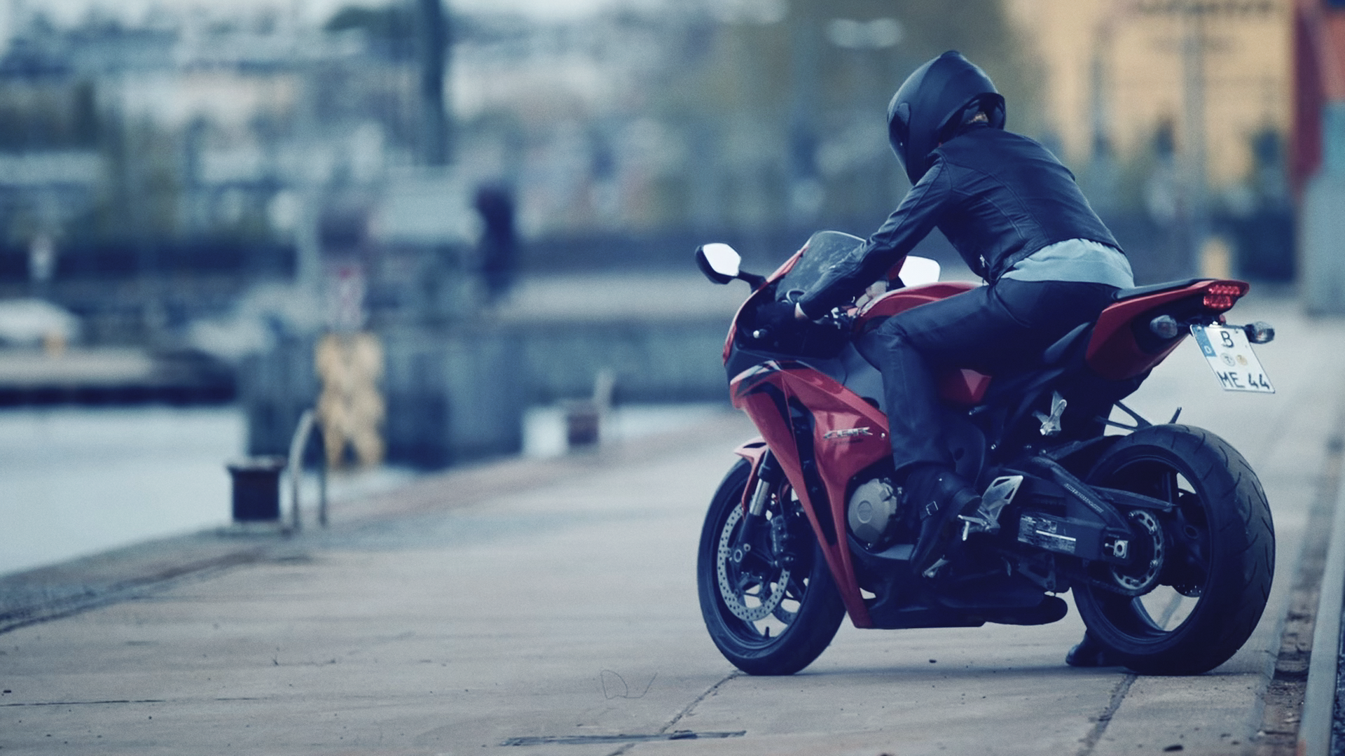 An einem Flussufer steht ein rotes Motorrad mit einem schwarzgekleideten Fahrer.