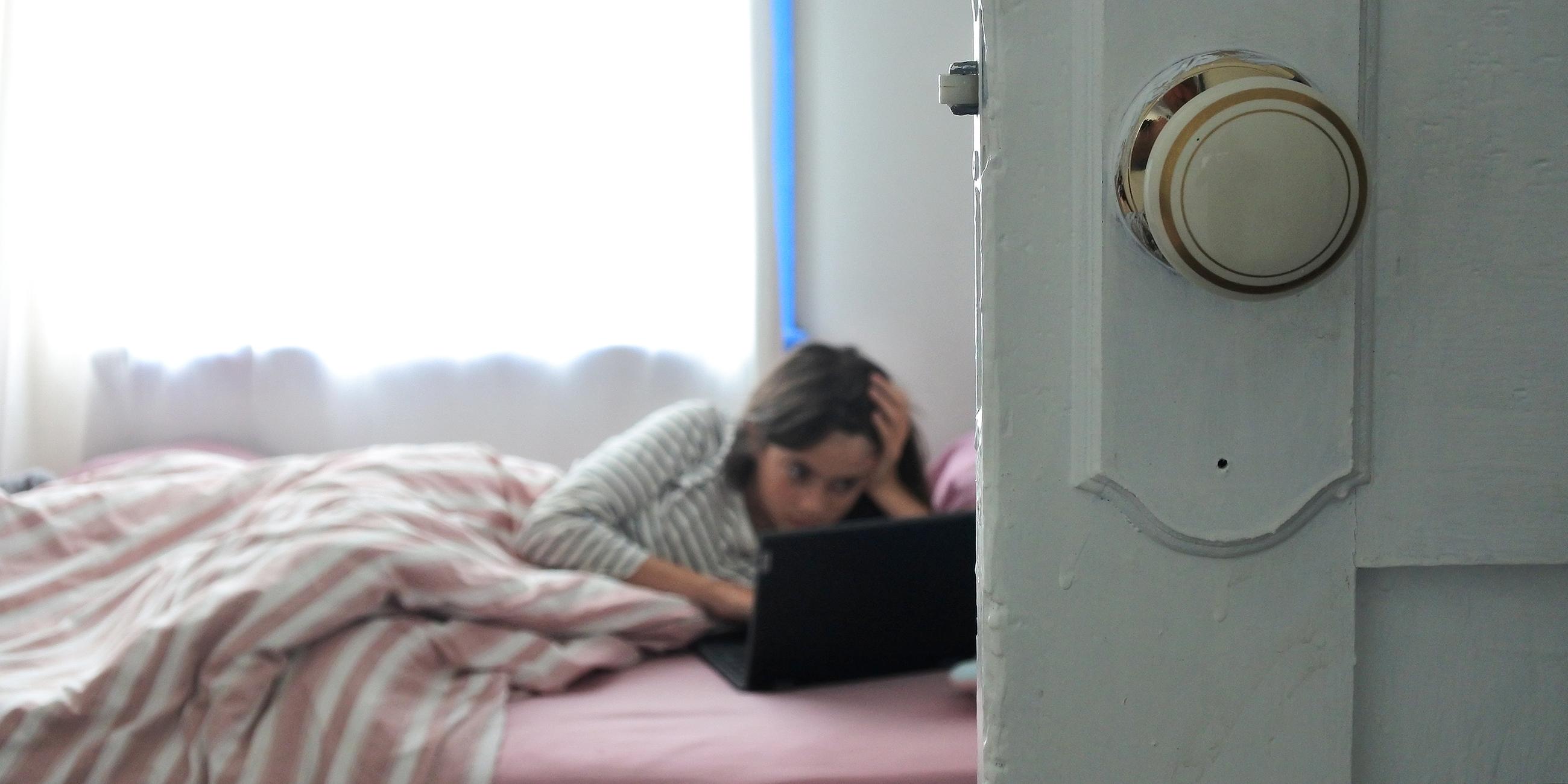 Ein junges Mädchen, das mit ihrem Laptop im Bett liegend im Internet surft, aufgenommen am 08.02.2022