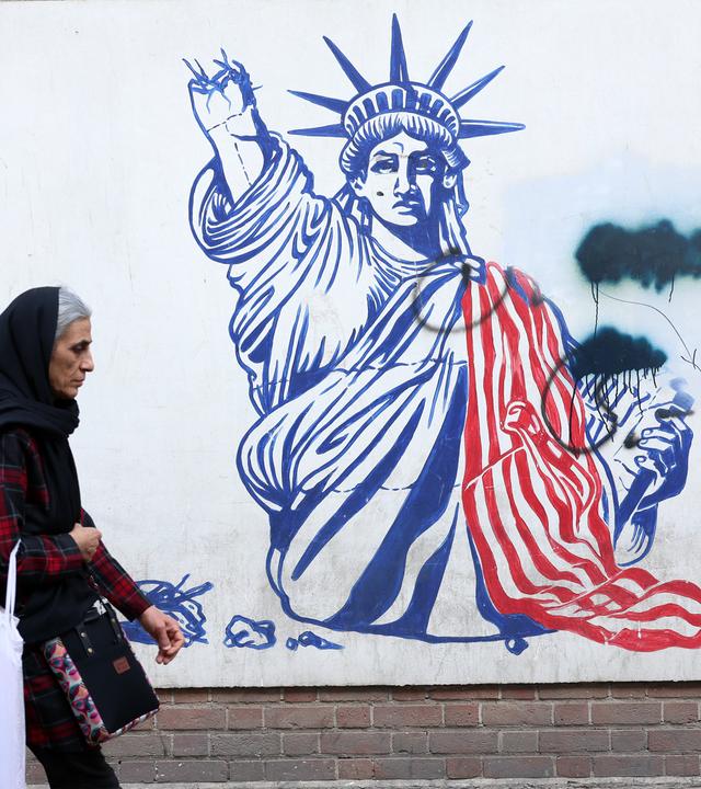 Frau mit Kopftuch geht an einem Wandbild vorbei. Darauf ist die Freiheitsstatue mit abgefetztem Arm zu sehen.