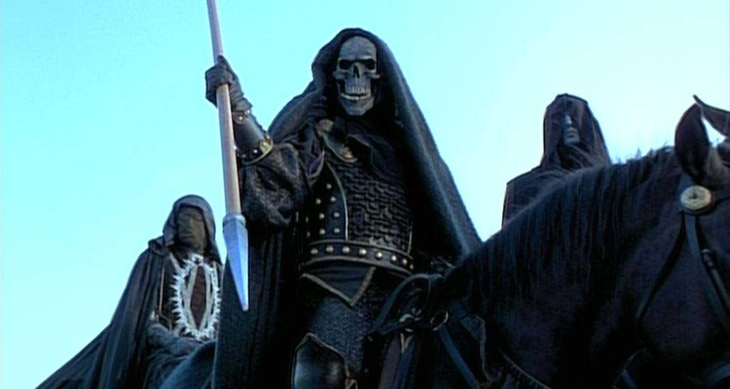 Drei Reiter auf schwarzen Pferden mit schwarzen Mänteln und Masken. Der Reitter in der Mitte trägt eine Totenkopfmaske und hält einen Speer in der Hand.