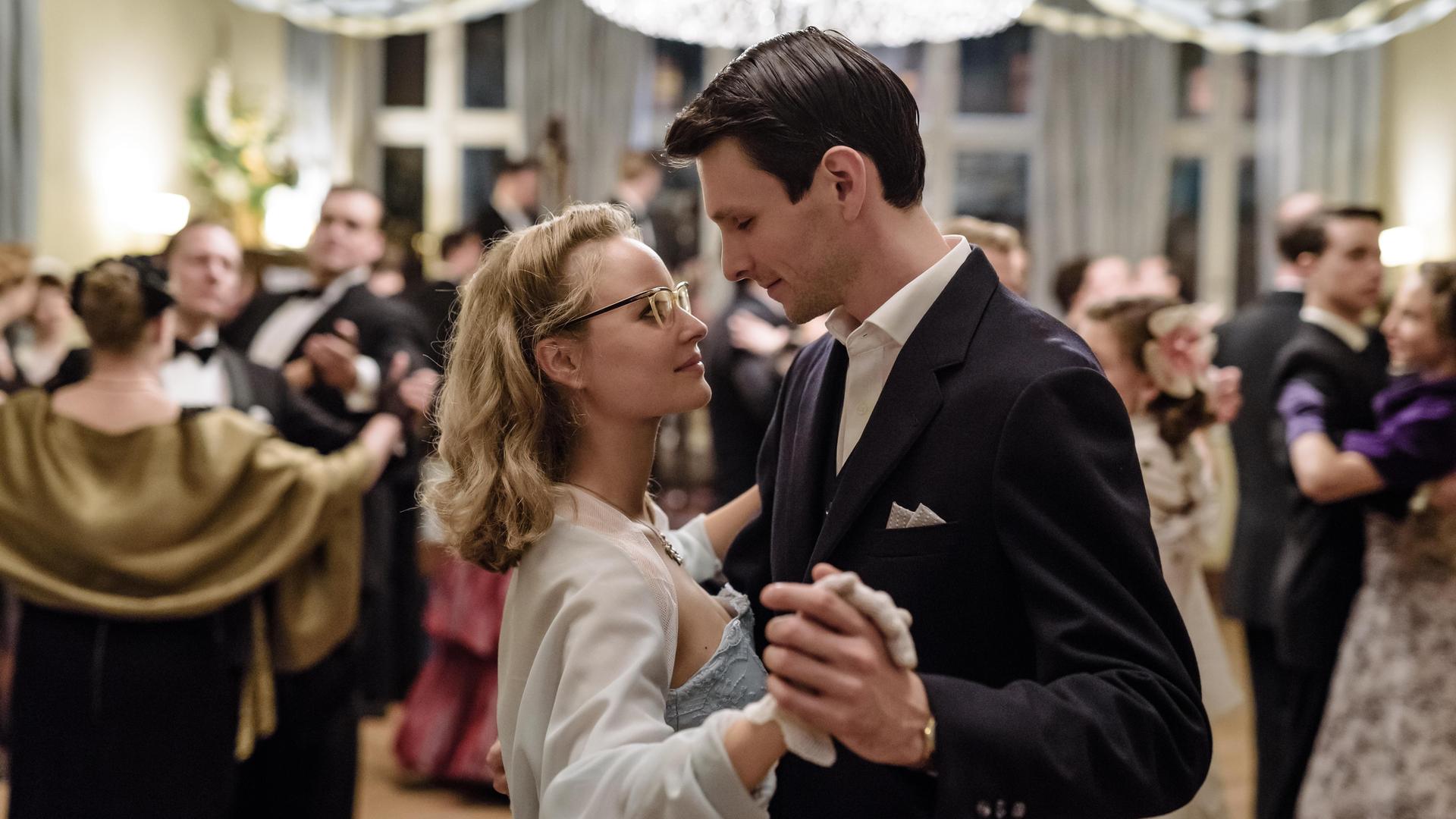 "Ku'damm 56 - Teil 3": Monika Schöllack (Sonja Gerhardt, mittig) und Freddy Donath (Trystan Pütter, rechts) tanzen auf dem Abschlussball der Tanzschule Galant Rock 'n' Roll. Um sie herum viele tanzende Menschen.