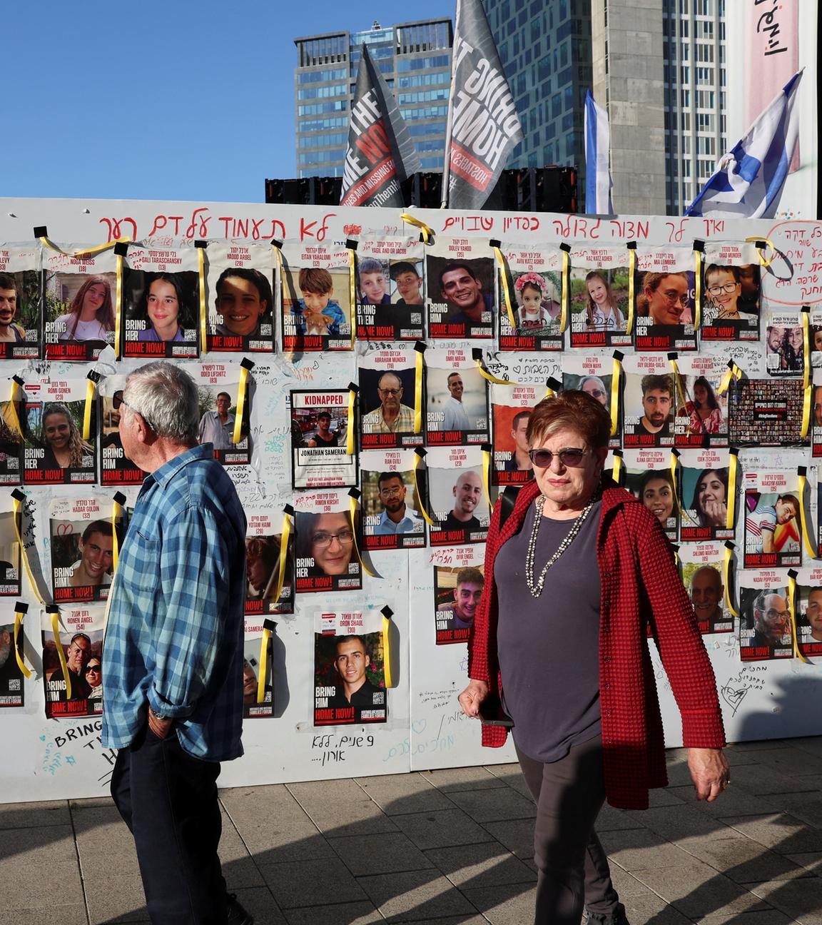 Menschen in Tel Aviv gehen am 30.11.2023 an einer Wand mit Plakaten vorbei, die vermisste Personen zeigt.