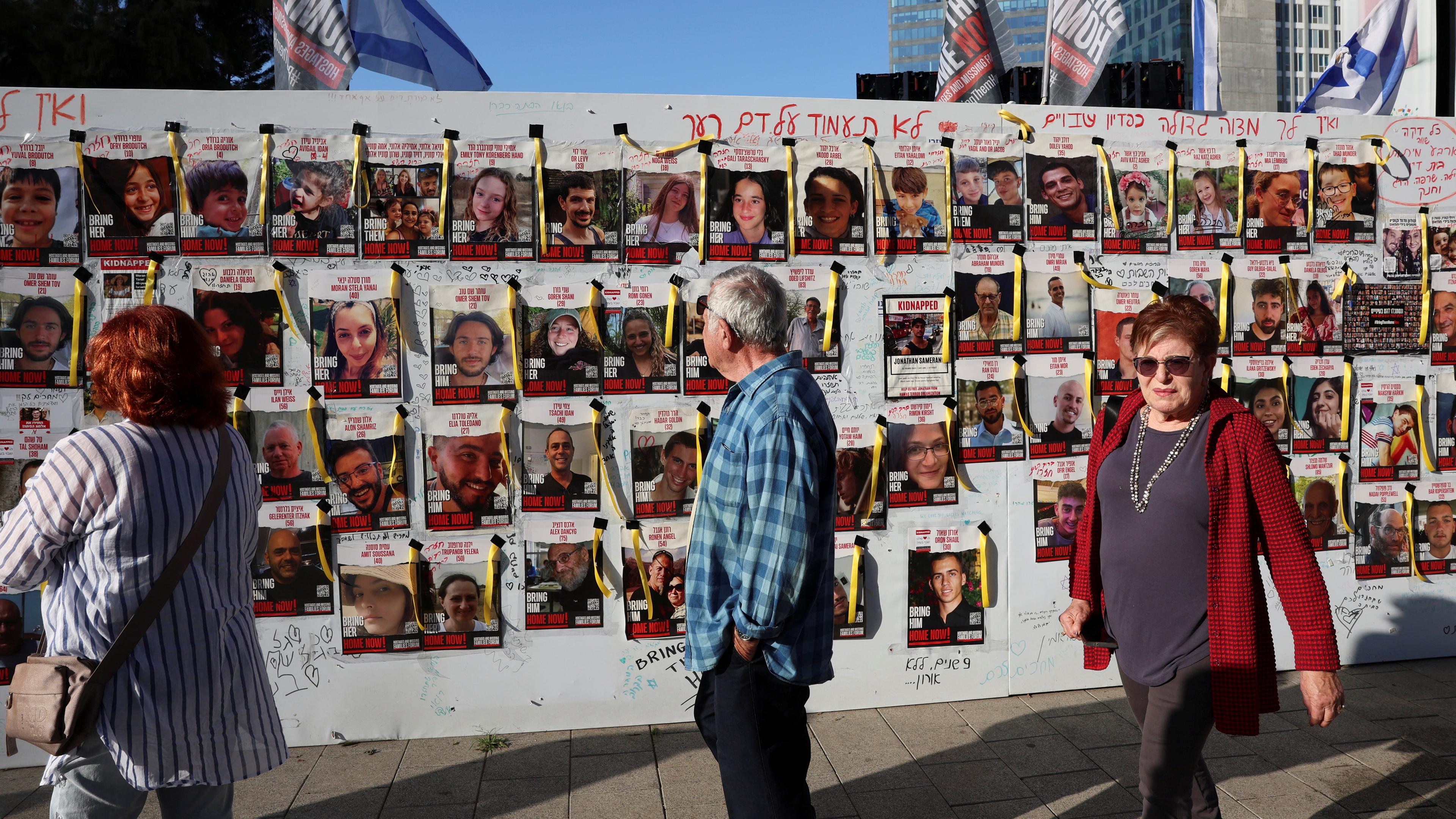 Menschen in Tel Aviv gehen am 30.11.2023 an einer Wand mit Plakaten vorbei, die vermisste Personen zeigt.