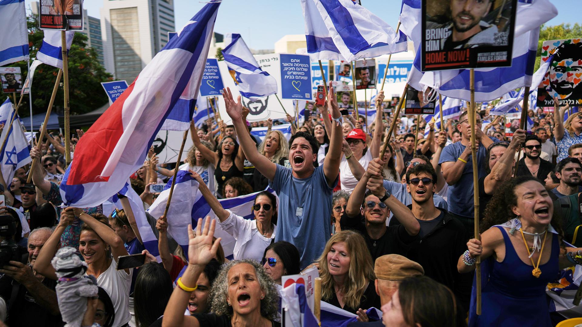 Auf einem Platz hat sich eine Menschenmenge versammelt, die weiß-blaue Fahnen schwenkt und jubelt.