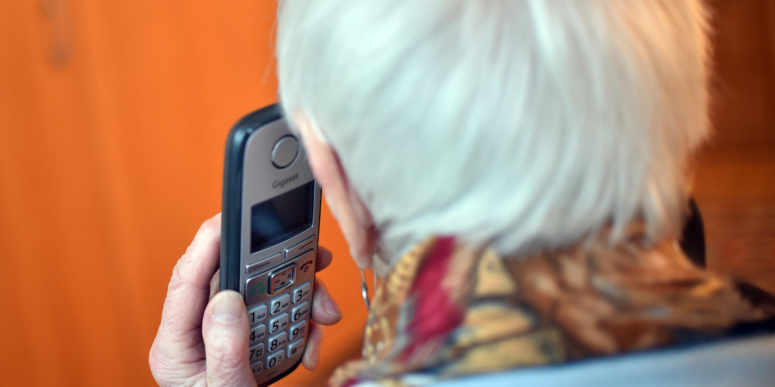 eine seniorin haelt einen telefonhoerer an ihr ohr (gestellte szene). im rahmen des projekts "silbernetz" wird einen hotline fuer einsame senioren angeboten.