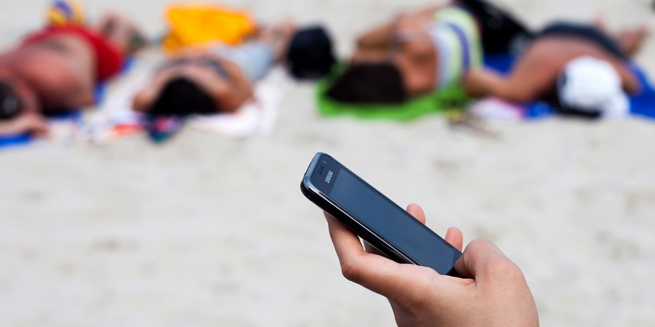 Archiv: Eine Frau schreibt mit einem Mobiltelefon eine SMs am Strand