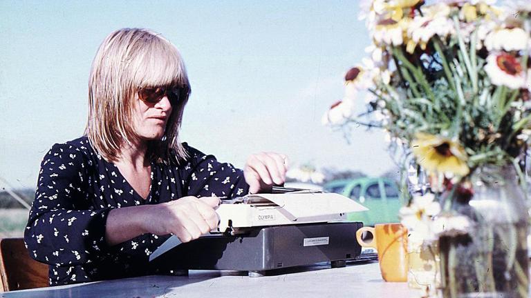 Die junge Frauenrechtlerin Alice Schwarzer sitzt mit Sonnenbrille im Freien an einer Schreibmaschine.