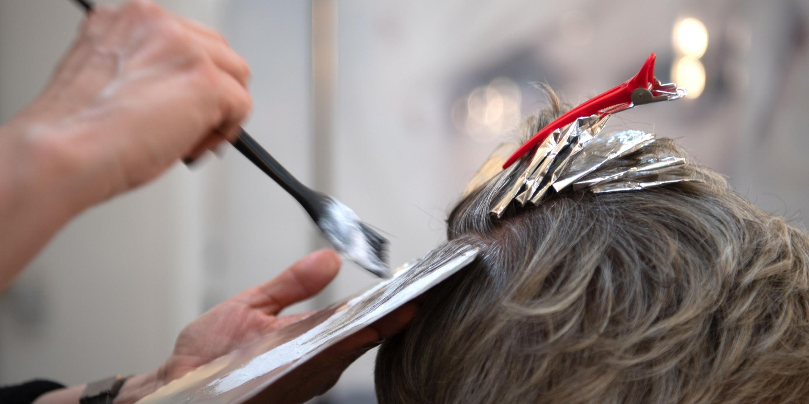 Friseurin färbt einer Kundin mit einem Pinsel die Haare. Symbol
