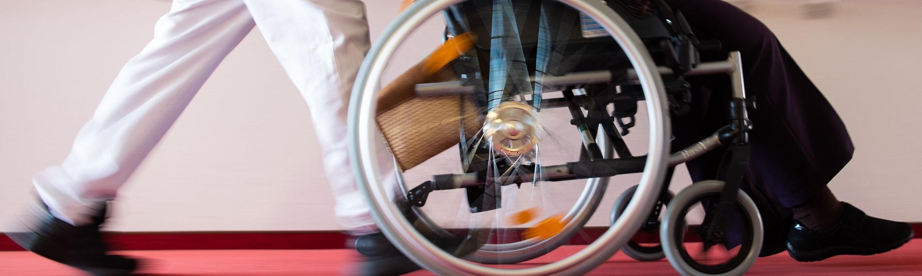 Pfleger schiebt einen Rollstuhl in einem Pflegeheim.