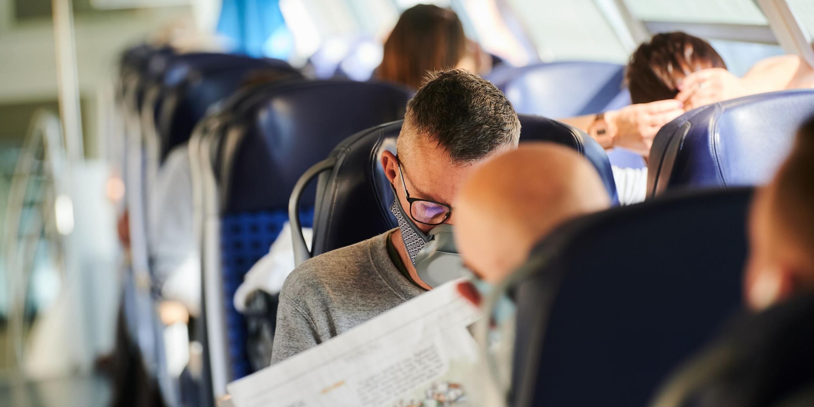 Reisende sitzen mit Nasen-Mund-Schutz in einem Zug. Symbolbild