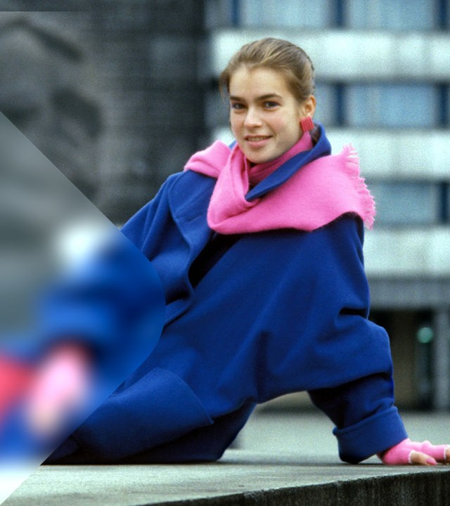 Kati Witt in einem blauen Mantel und rosanen Schal vor der großen Statue von Karl Marx.