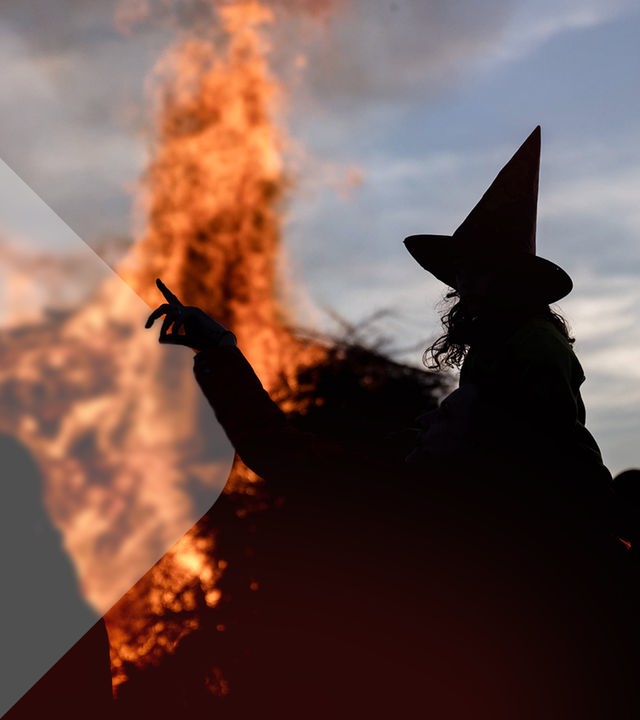 Eine als Hexe verkleidete Frau vor einem Lagerfeuer. 