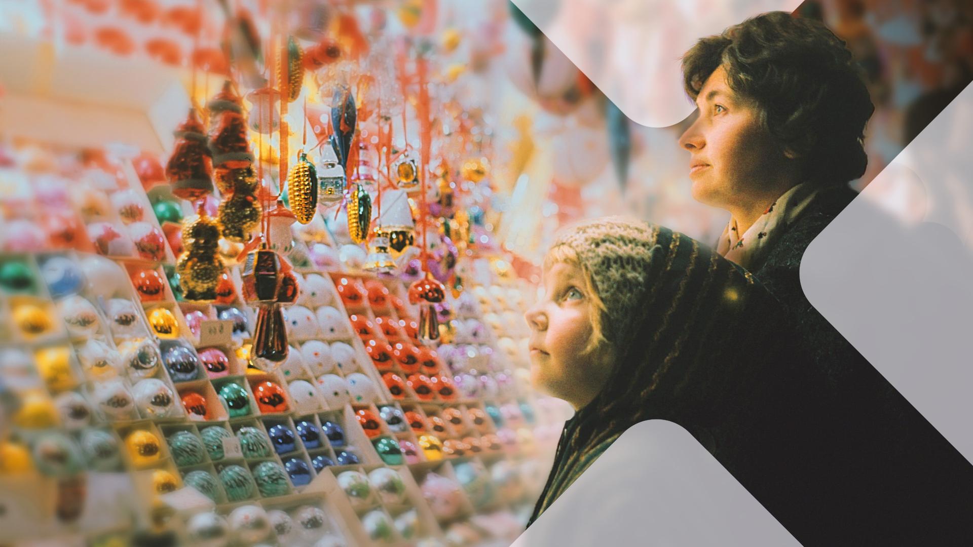 Ein kleines Kind und seine Mutter vor einem Stand mit bunten Christbaumkugeln auf dem Weihnachtsmarkt.