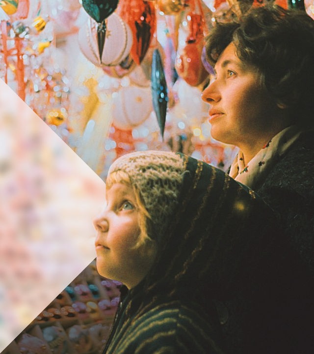 Ein kleines Kind und seine Mutter vor einem Stand mit bunten Christbaumkugeln auf dem Weihnachtsmarkt.