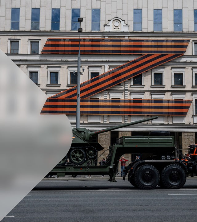 Ein Panzer fährt eine Straße entlang, im Hintergrund an der Hauswand ein großes, rotes Z als Symbol der russischen Streitkäfte. 