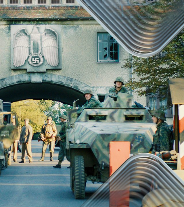Szenisches Foto, das den Eingang der Zittwerke samt militärischem Sperrposten zeigt. Im Hintergrund sind Wachpersonal, KZ-Häftlinge  und Militärfahrzeuge zu sehen. Grafisch bearbeitet im Terra X-Look.