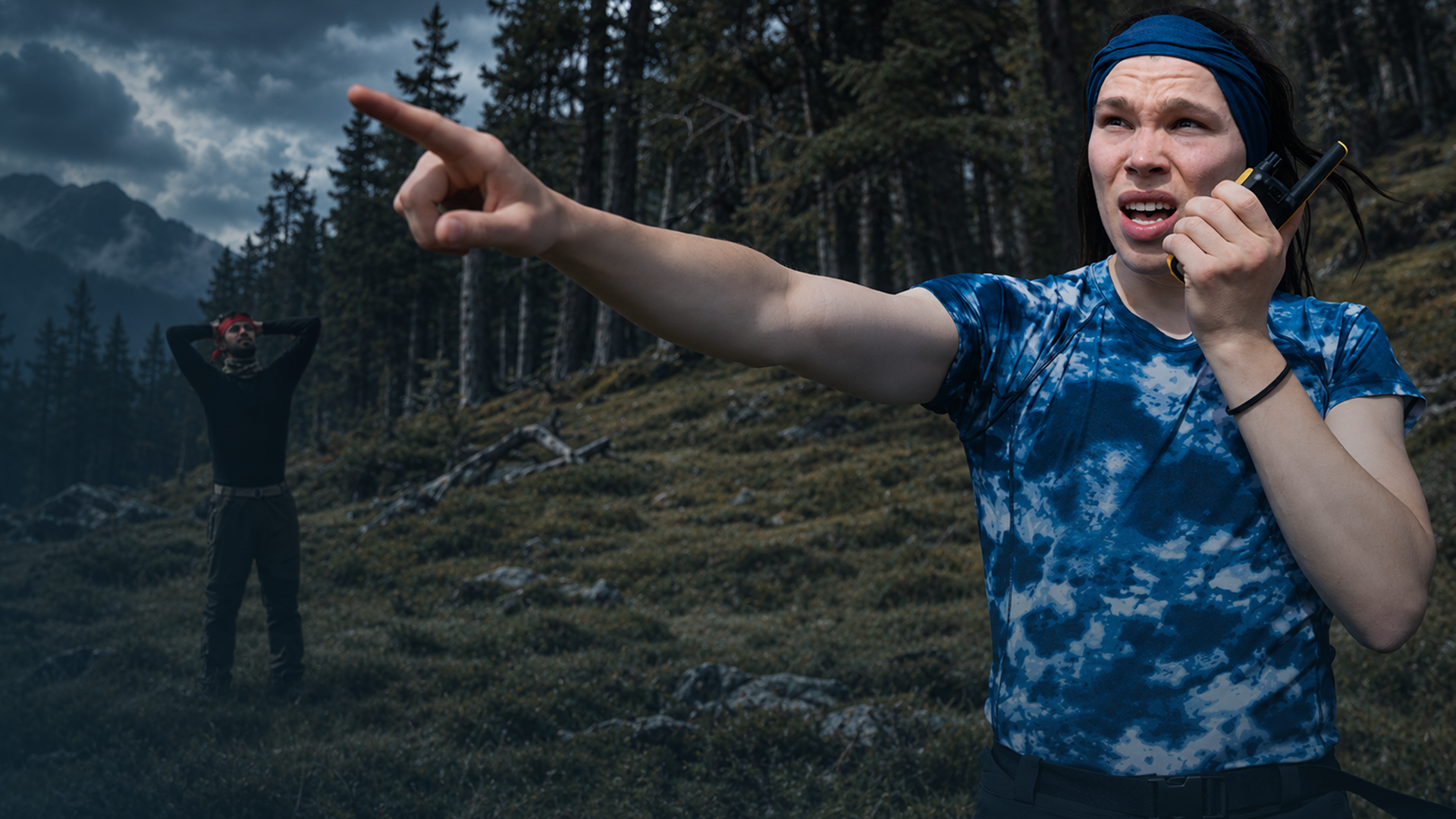 Lézan und Helge Mark stehen auf einem bewaldeten Hügel unter dunklen Wolken. Helge Mark befindet sich rechts im Vordergrund, trägt ein blau T-Shirt und ein blaues Stirnband. Er spricht in ein Funkgerät und zeigt mit ausgestrecktem Arm nach links. Weiter hinten steht Lézan mit einem roten Stirnband. Er hat beide Hände hinter dem Kopf verschränkt.