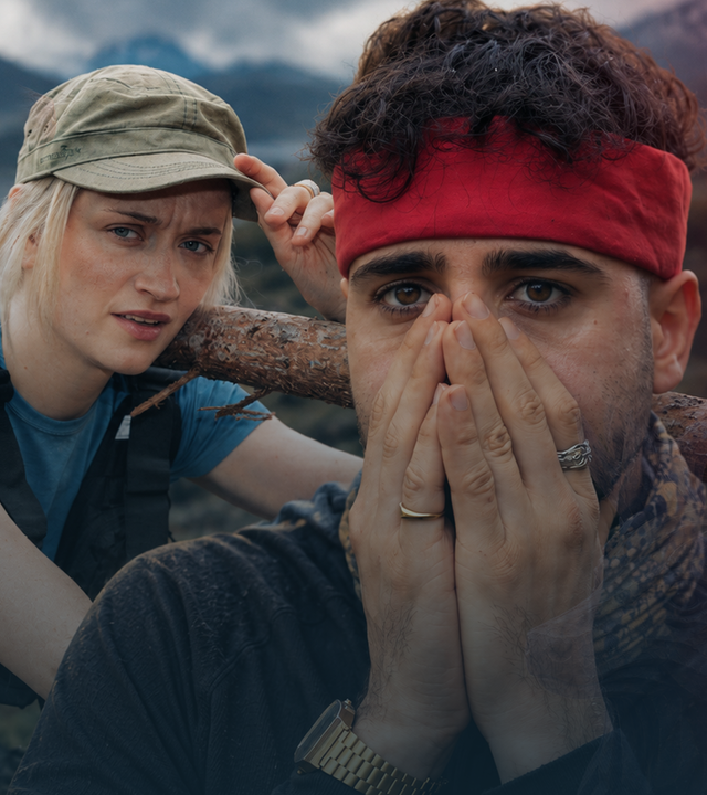Merleperle steht links neben Lézan und trägt eine Flagge auf der Schulter. Sie trägt ein blaues Shirt und sieht erschöpft aus. Lézan trägt ein rotes Stirnband und hält beide Hände erschrocken vor den Mund.