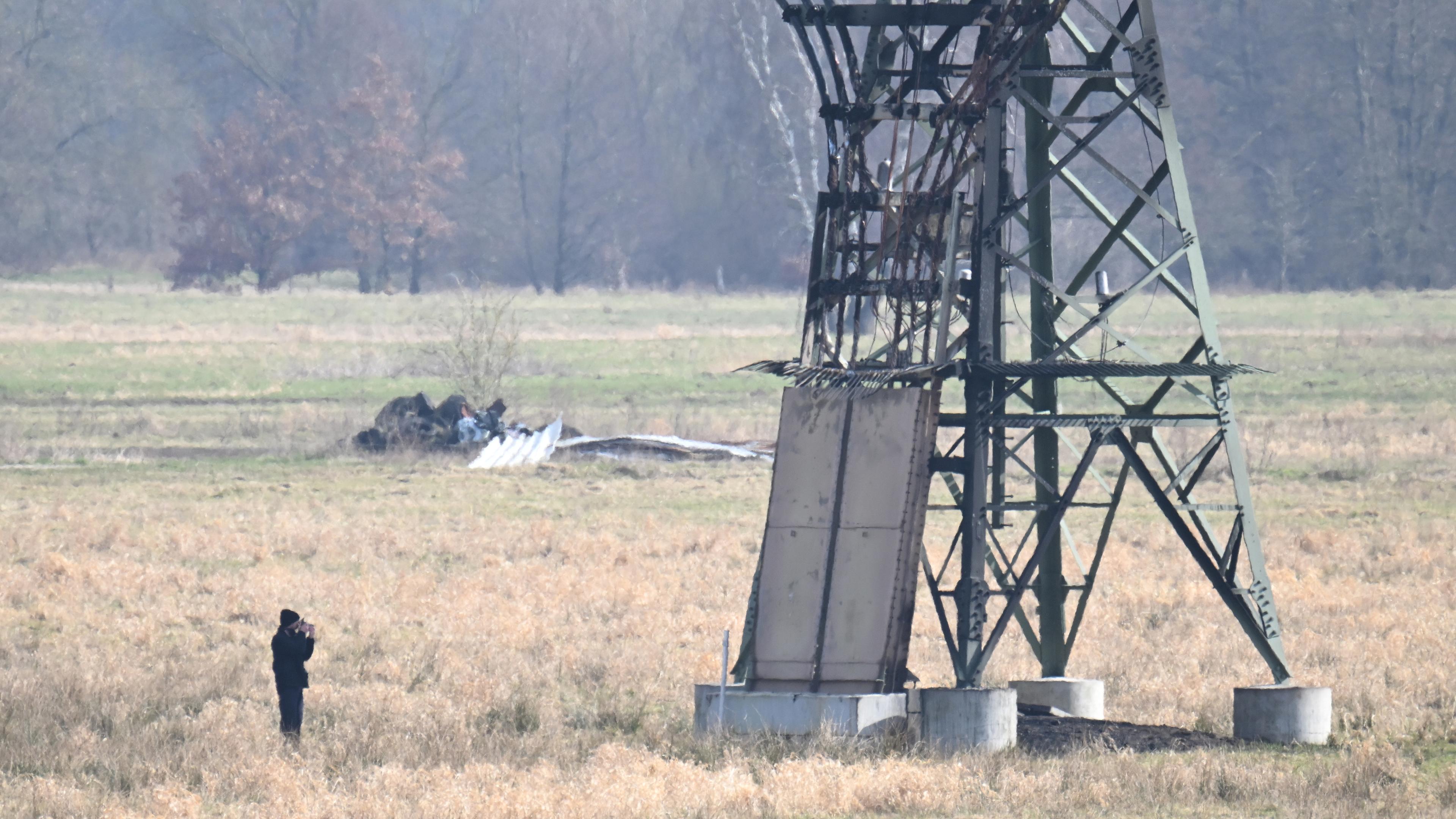 Brandenburg, Spreenhagen: Ein verbrannter Strommast steht auf einem Feld und ein Polizeifotograf dokumentiert die Spuren.