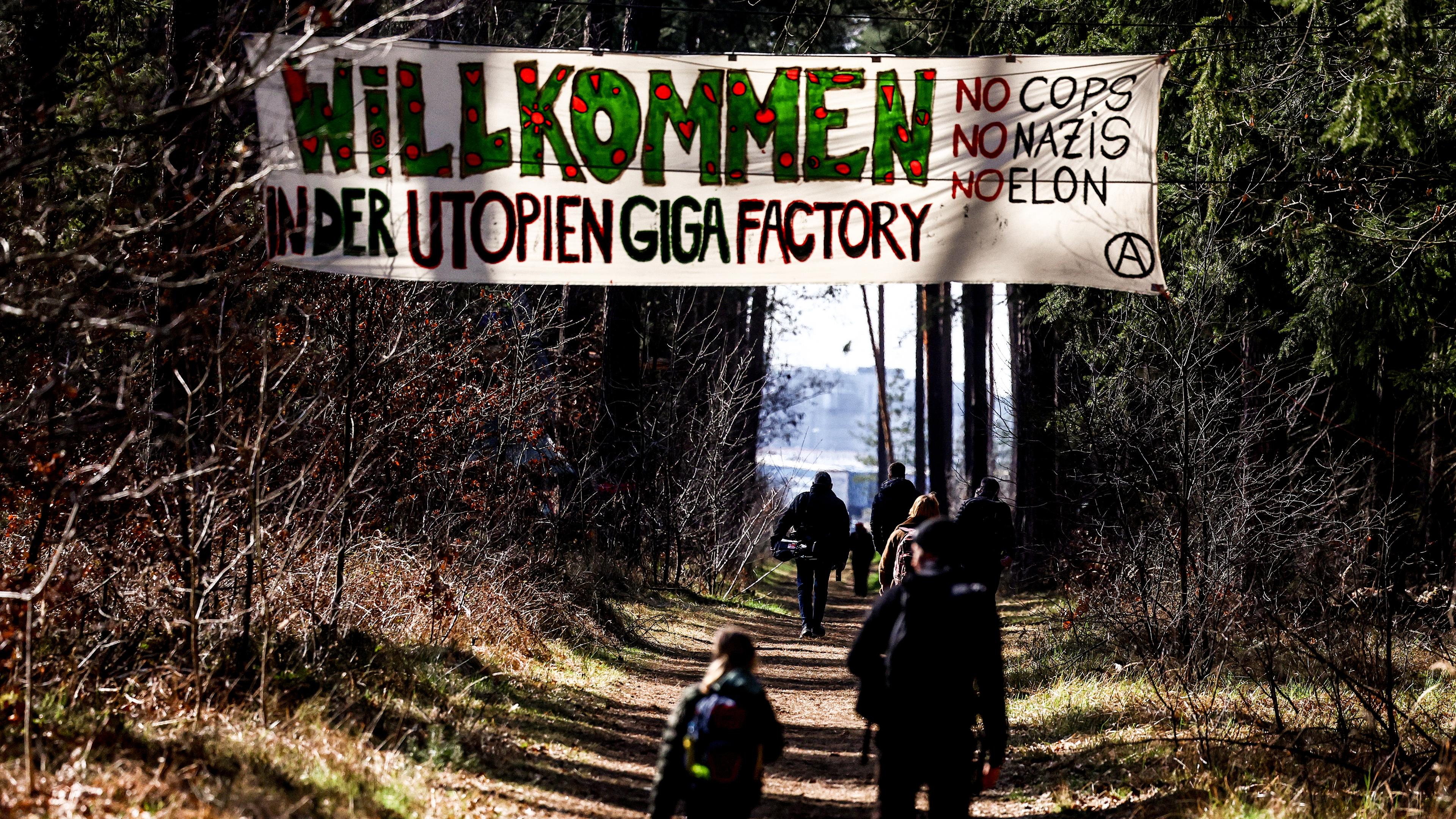 Umweltaktivistinen zeigen ein Banner mit der Aufschrift: "Willkommen in der Utopien Giga Factory" während eines Protestes gegen die Waldrodung zum Ausbau der Tesla Gigafactory in Grünheide.
