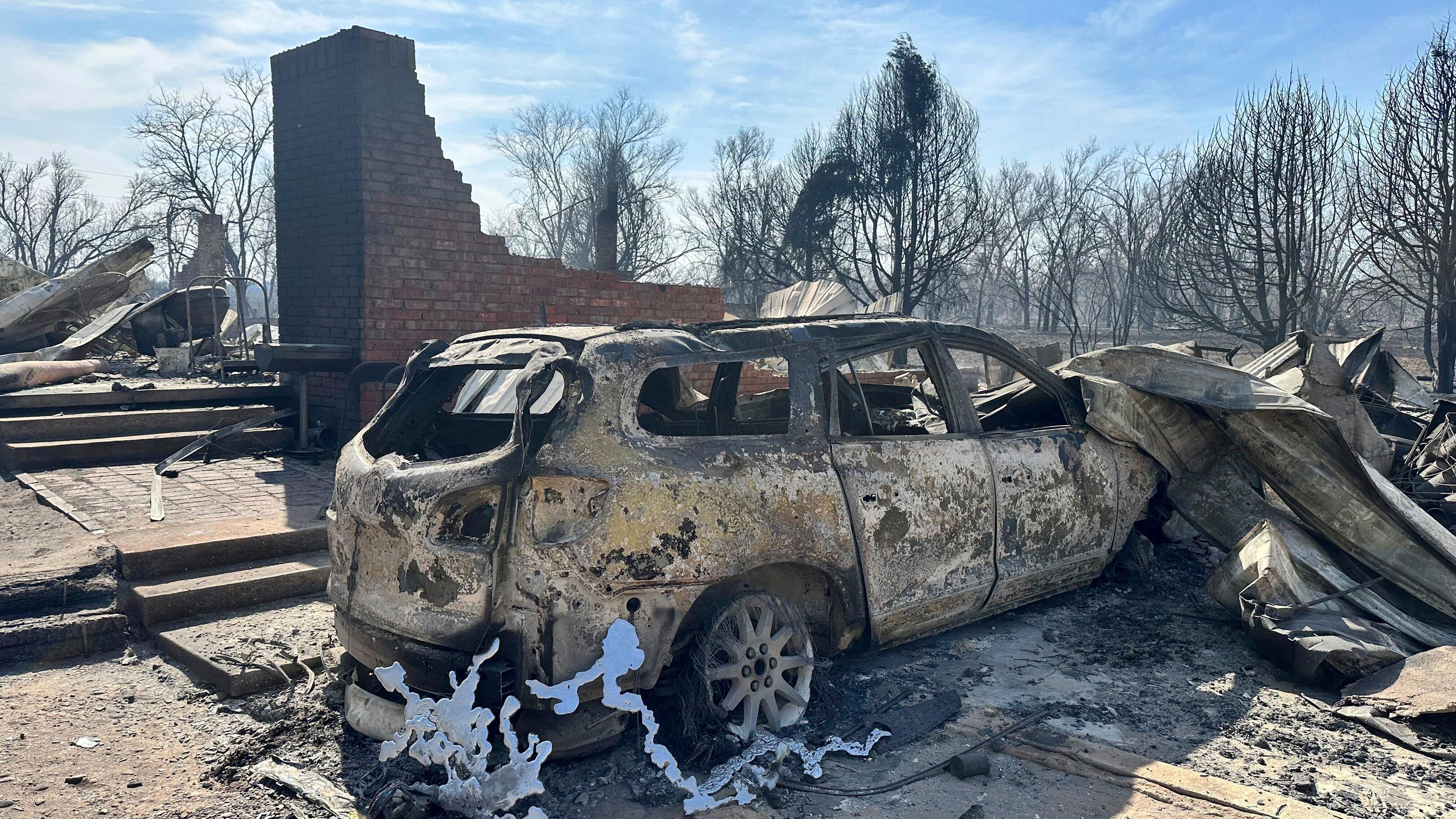 Archiv, 28.02.2024, USA, Canadian: Ein verbranntes Auto steht in der Nähe der verkohlten Überreste eines Hauses außerhalb von Canadian, nachdem ein Waldbrand vorbeigezogen war. 